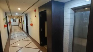A long, well-lit hallway with tiled flooring, multiple doors, and potted plants. - Hotel Grand Ambience (Gandhidham)