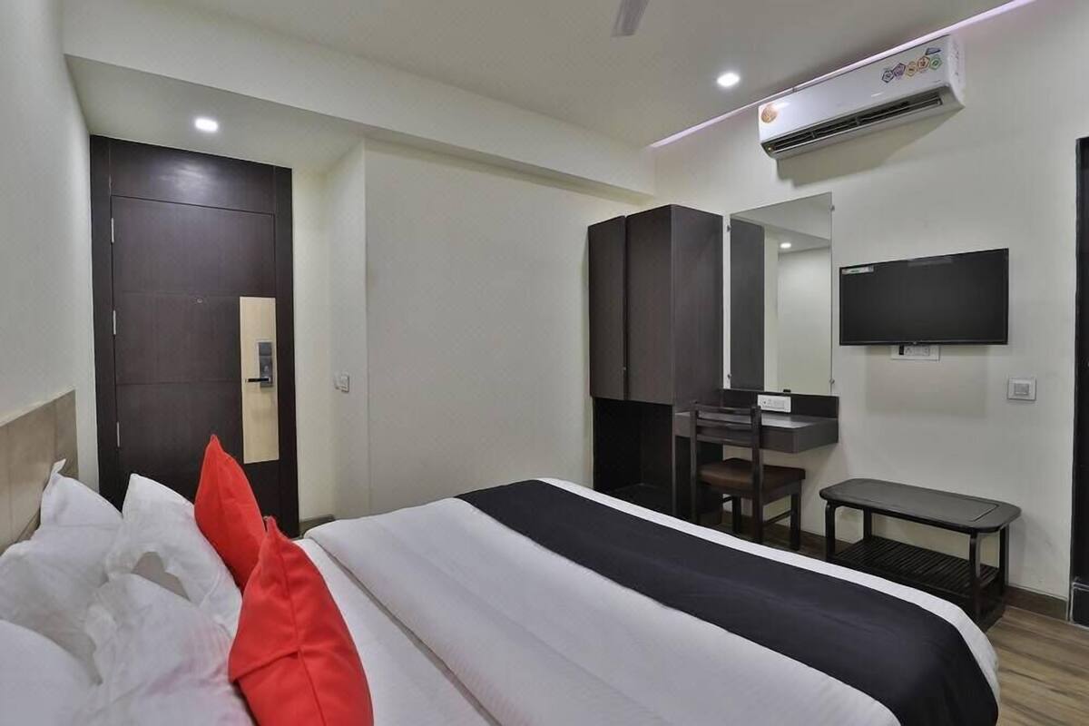 A hotel room with a bed, a desk, a chair, a TV, and an air conditioning unit.