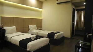 A hotel room with two beds, a small table, and an air conditioning unit. - Hotel Grand Ambience (Gandhidham)