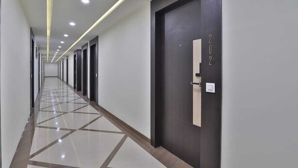 A long, narrow hallway with a geometric patterned floor, recessed ceiling lighting, and a dark-colored door with the number 202 visible. - Hotel Grand Ambience (Gandhidham)