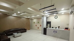 A modern reception area with a reception desk, a clock, and a seating area with a sofa and a coffee table. - Hotel Grand Ambience (Gandhidham)