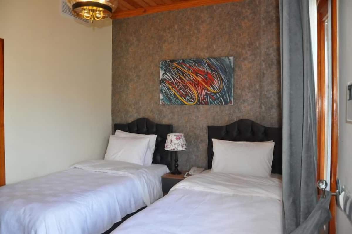 Habitación de hotel con dos camas, una mesita de noche con lámpara y un cuadro abstracto de colores en la pared.