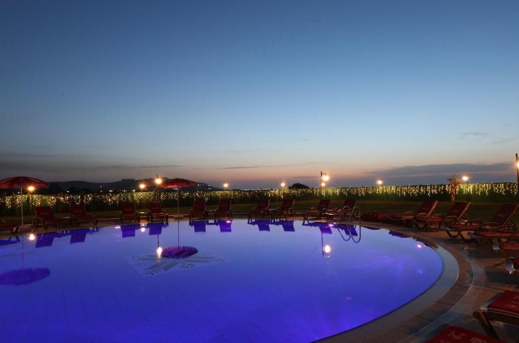 Una piscina con sillas de descanso y sombrillas, rodeada de luces y vistas al paisaje.