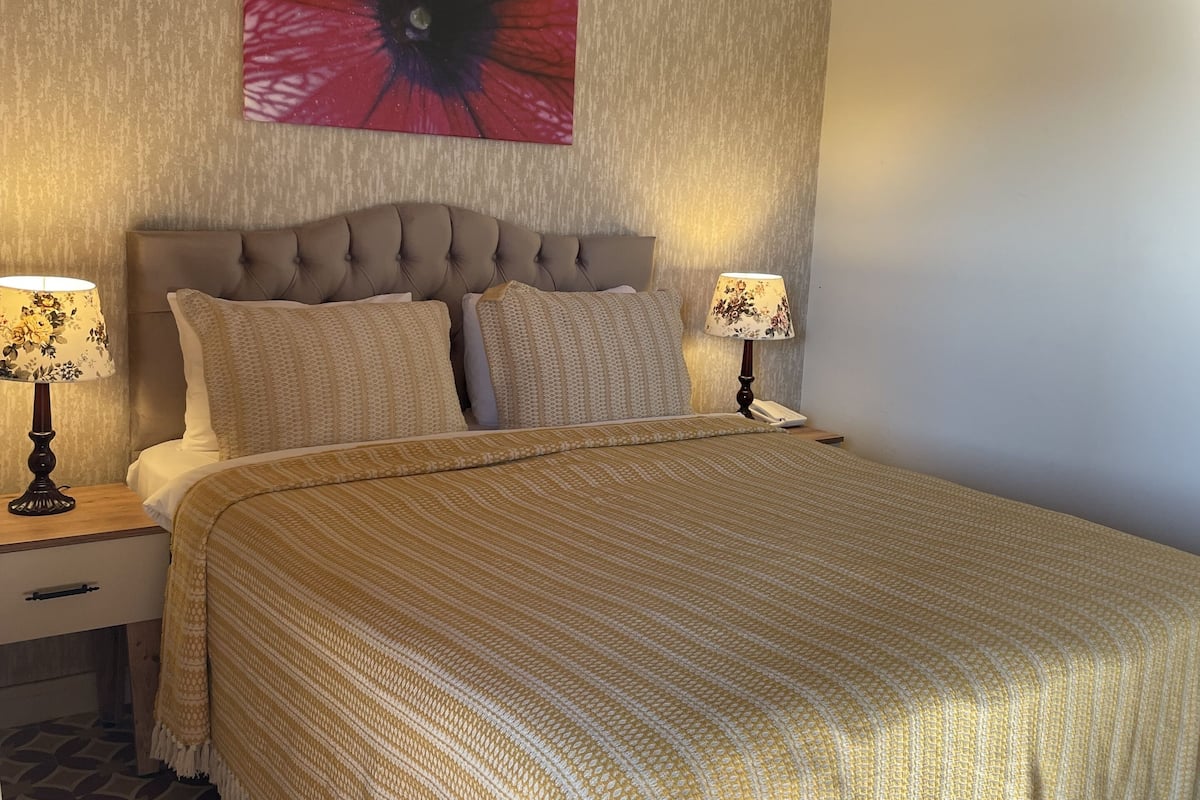 Un dormitorio con una cama grande, dos mesitas de noche con lámparas, un tapiz decorativo y baldosas de suelo estampadas.