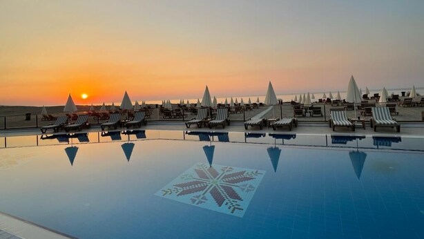 A pool with lounge chairs and umbrellas, a sunset in the background, and a geometric pattern on the pool's surface. - Tarihi Kumbaba Otel (Sile)