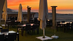 An outdoor dining area with tables and umbrellas, overlooking a beach at sunset. - Tarihi Kumbaba Otel (Sile)