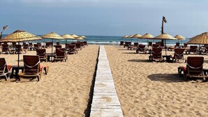 A beach with rows of sun loungers and thatched umbrellas, a wooden walkway leading to the sea. - Tarihi Kumbaba Otel (Sile)
