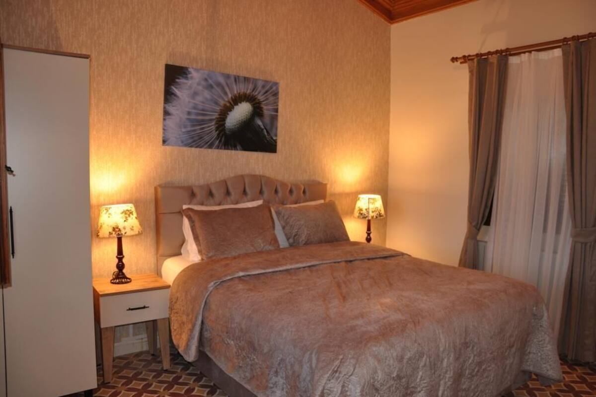 Un dormitorio con una cama, dos lámparas de noche, una mesita de noche, una puerta y un cuadro colgado en la pared.