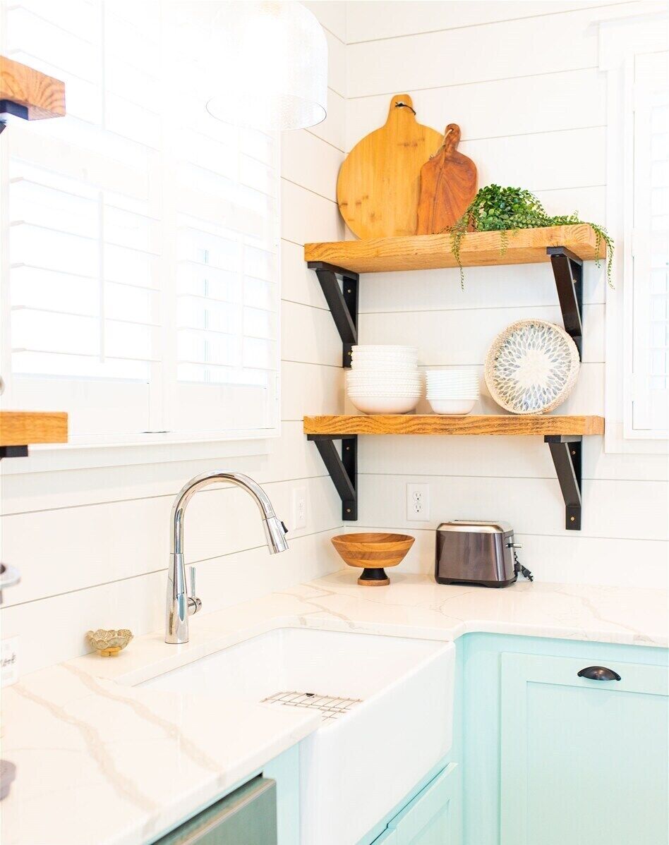 A kitchen with white subway tiles, a stainless steel sink, a toaster, and wooden shelves with dishes and a plant.