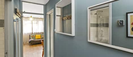 A hallway with a shower area, a door leading to a living room, and a light fixture on the ceiling.
