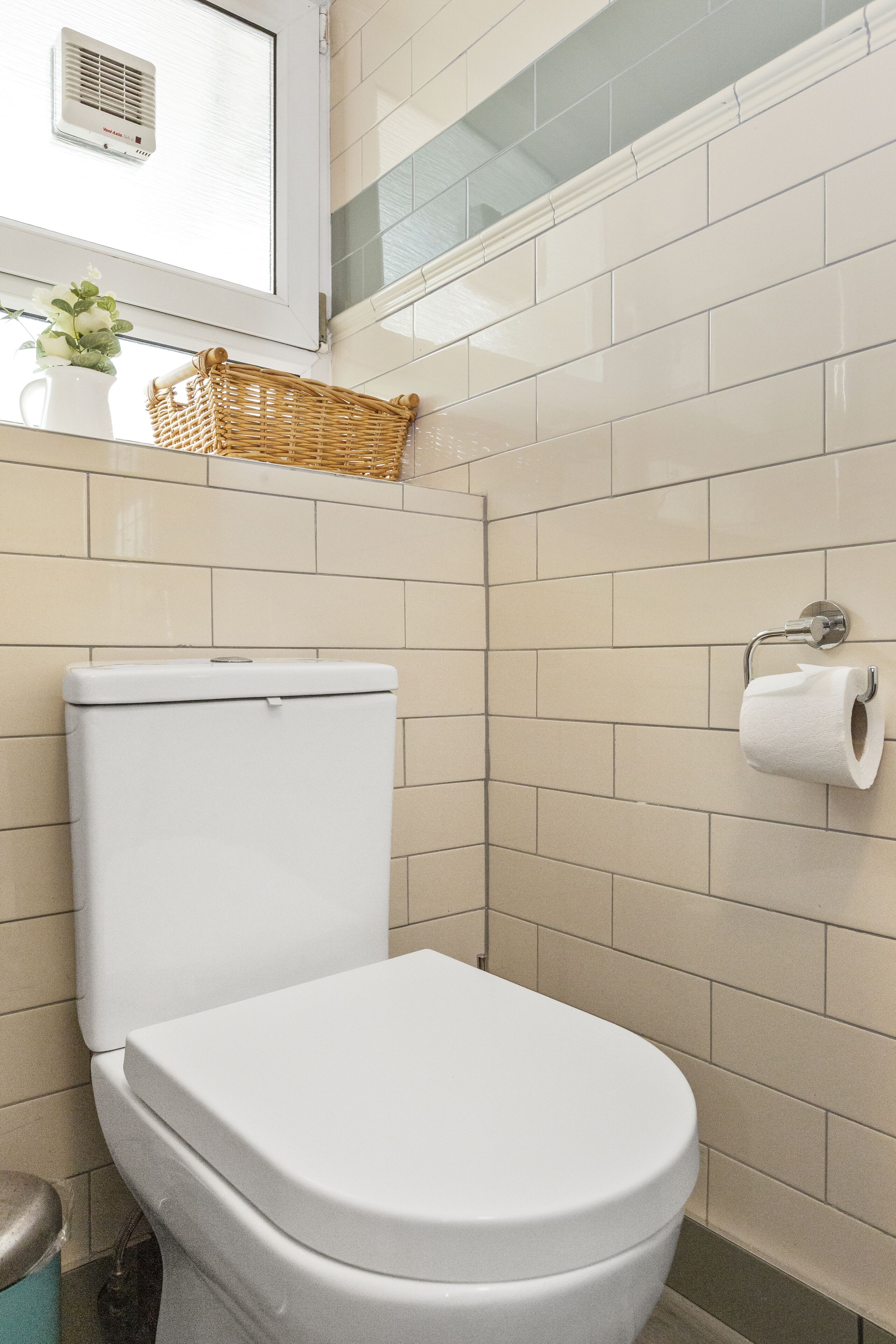 A bathroom with a white toilet, a wall-mounted toilet paper holder, and a wicker basket on the wall.