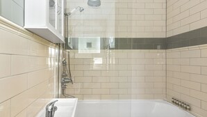 A bathroom with a bathtub, a shower, and a sink with a faucet and soap dispenser. - Stylish 1BR Next to Tower Bridge (London)