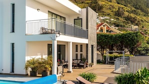 A modern two-story building with a balcony, outdoor seating area, and a pool.