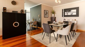 A dining area with a table set for four, surrounded by chairs, a vase with flowers, and a framed picture on the wall.