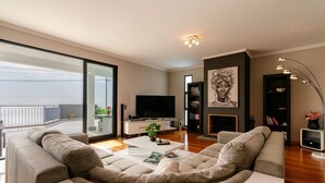 A modern living room with a large sectional sofa, a flat-screen TV, a fireplace, and a bookshelf.