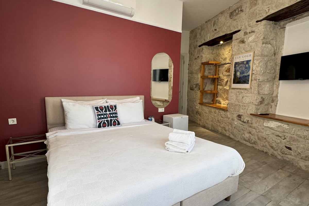 A bedroom with a large bed, a chandelier, a stone wall, and a mounted TV.