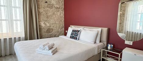 A hotel room with a large bed, a stone wall, a red accent wall, a chandelier, and a small table with a mirror.