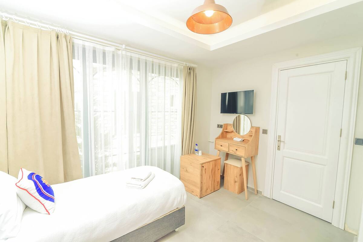 A hotel room with a bed, a wooden desk, a mirror, and a television on the wall.