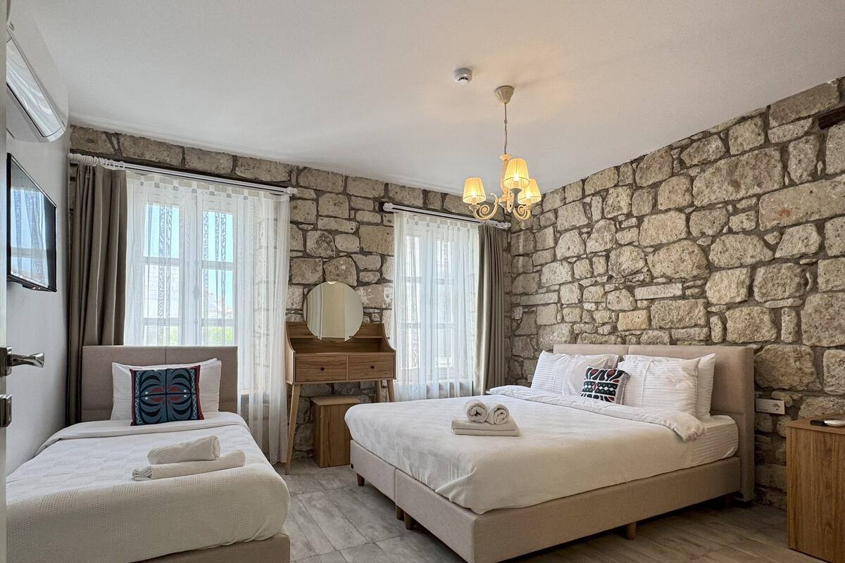 A room with two beds, a desk, and a stone wall.