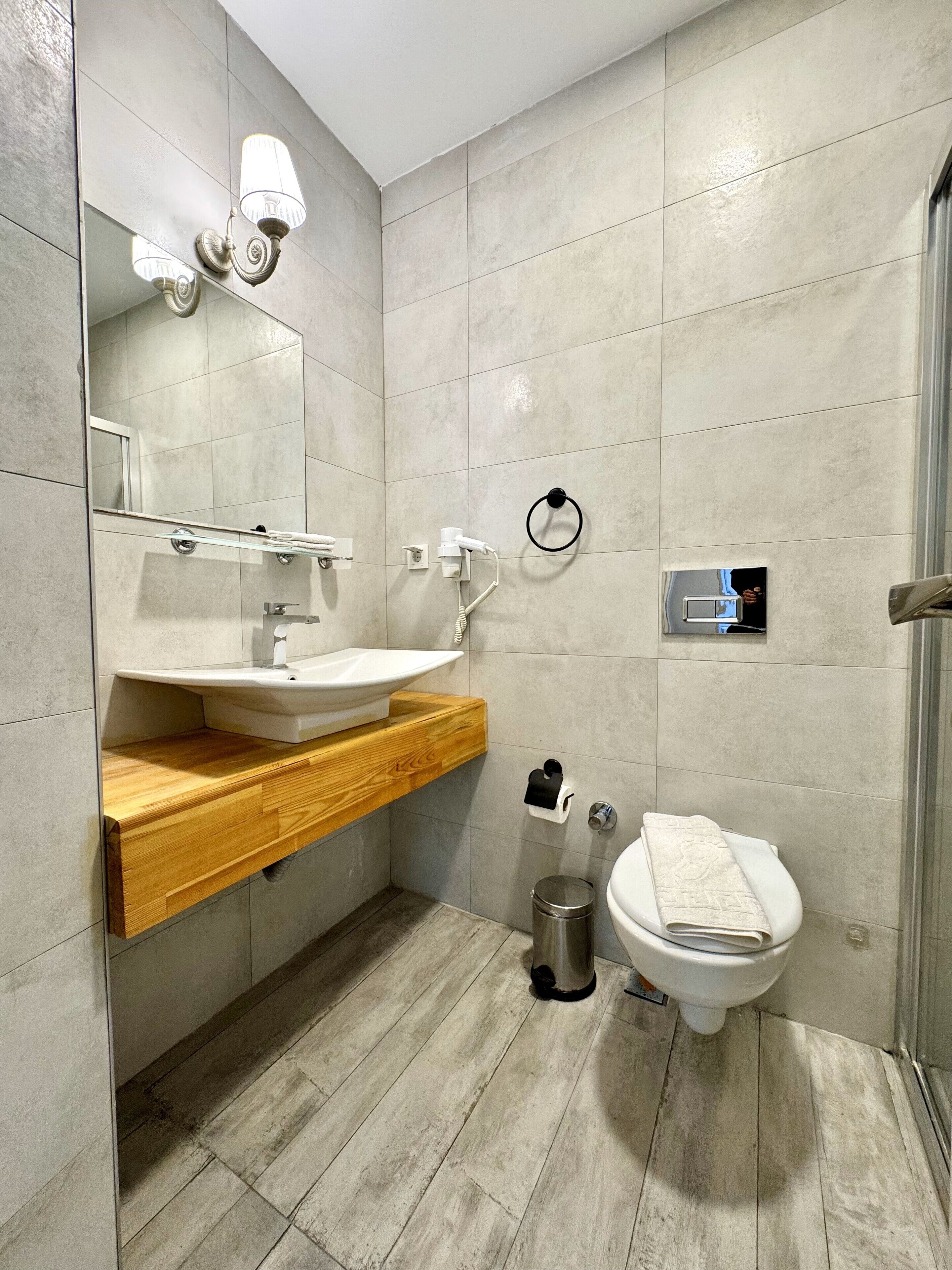 Une salle de bain moderne avec un meuble-lavabo en bois, un lavabo blanc, un miroir, un porte-serviettes, des toilettes et un espace douche.
