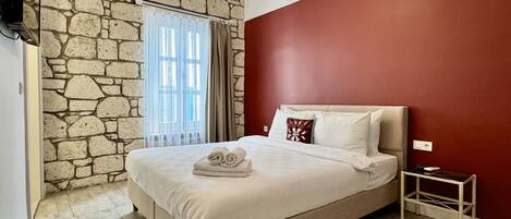 A bedroom with a stone wall, a bed with white linens, a red accent wall, and a ceiling light fixture.