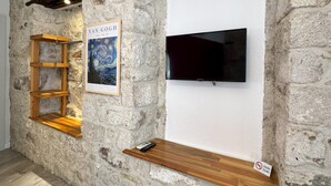 Paredes de pedra com uma televisão montada, prateleiras de madeira e uma obra de arte emoldurada.