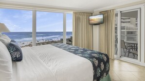 Habitación de hotel con una cama grande, un televisor montado en la pared y vistas a la playa y al océano.