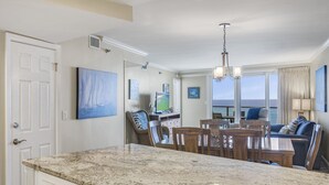 Una cocina con encimera de granito, sillas de madera y una mesa de comedor. Hay un ventanal con vista al océano.