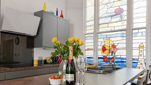 Une cuisine avec une grande fenêtre, une bouteille de vin et un saladier rempli de fruits.