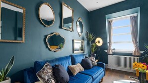 Una sala de estar con un sofá azul, varios espejos, un radiador y una ventana con cortinas.