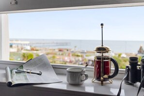 Une vue sur un paysage urbain à travers une fenêtre, avec une machine à café, une tasse et des jumelles posés sur une table.