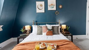 Un dormitorio con cama, mesitas de noche, una bandeja con desayuno y decoración en la pared.