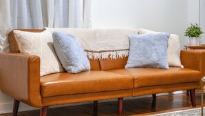 A brown leather sofa with two light blue pillows and a white throw blanket.