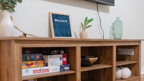 A wooden entertainment center with board games, a welcome sign, a plant, and a vase.