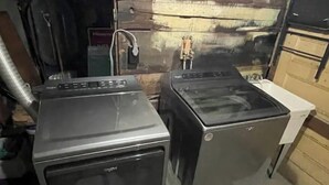 Two stacked washing machines in a room with a concrete floor and wooden walls.