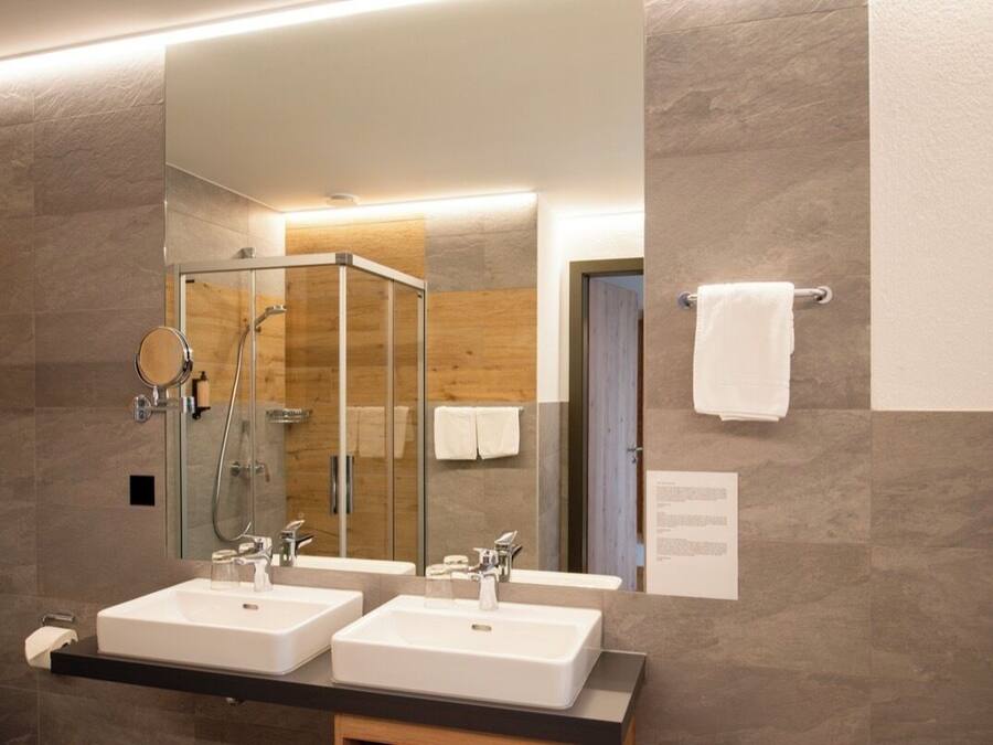 Une salle de bain moderne avec deux lavabos, une douche à l’italienne en verre et un grand miroir.