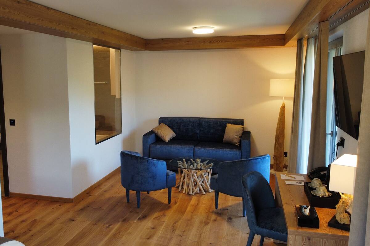 A modern living room with a blue sofa, two armchairs, a glass coffee table, and a wooden floor.