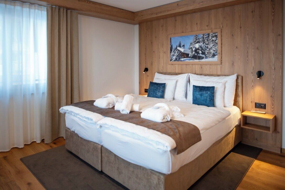 A large bed with a wooden headboard, a painting of a snowy landscape, and a nightstand with a lamp.