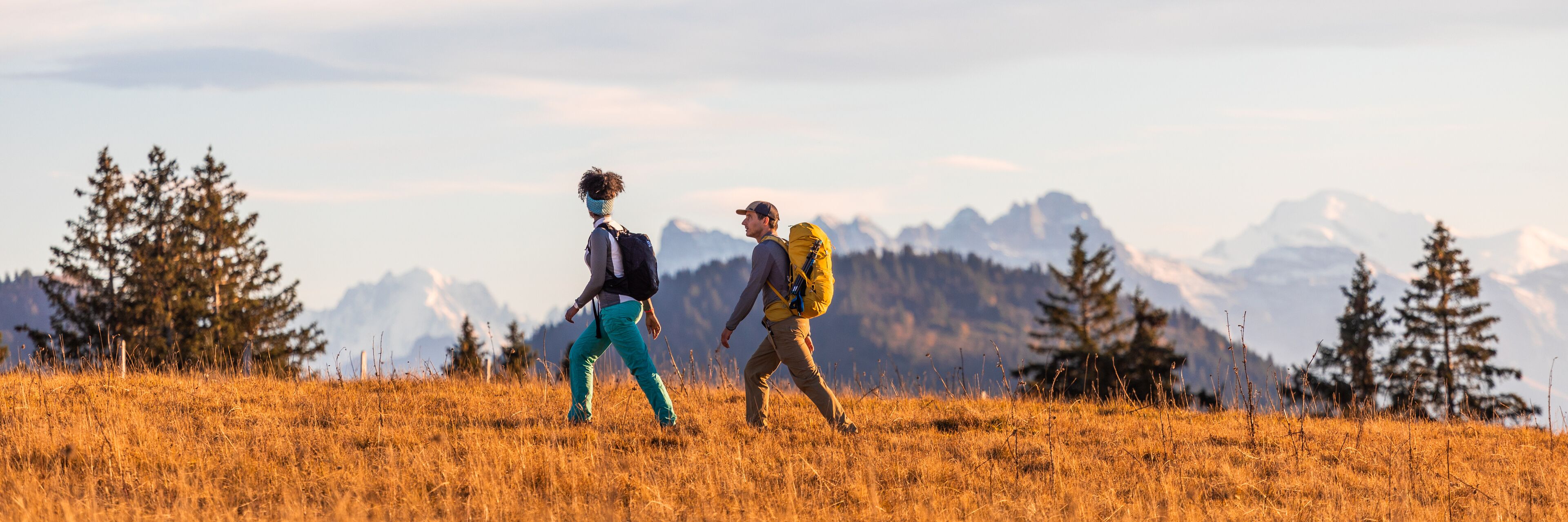 Dos excursionistas caminando por un campo de hierba con montañas al fondo.