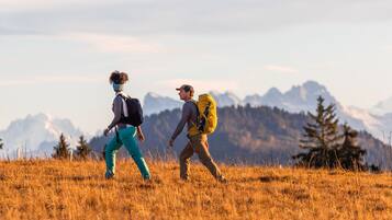 Dos excursionistas caminando por un campo de hierba con montañas al fondo.
