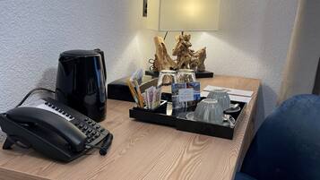 A hotel reception desk with a telephone, a black coffee maker, a tray with magazines, a small wooden sculpture, and a mirror on the wall.