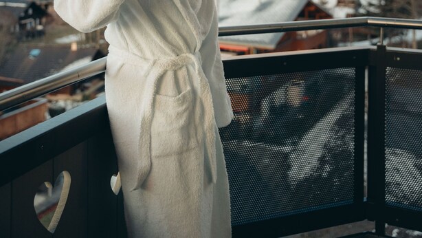 A person in a white bathrobe standing on a balcony with a mountain view in the background. - Boutique Hôtel Corbetta (Chatel-Saint-Denis)