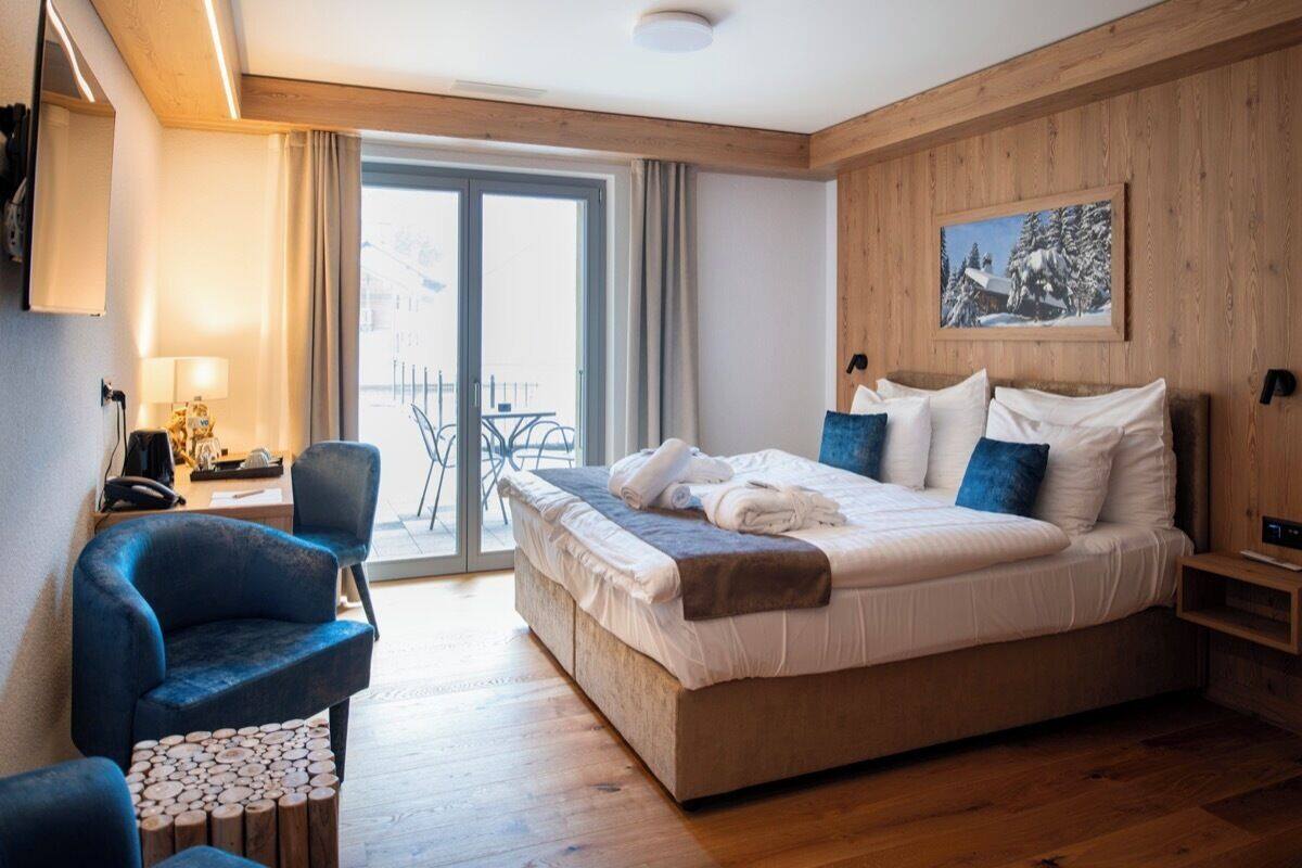 A hotel room with a large bed, a desk with a chair, a small round table, and a view of the outdoors through a sliding door.