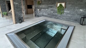 A modern indoor pool area with a rectangular pool, stone walls, and a ceiling with a perforated design. - Boutique Hôtel Corbetta (Chatel-Saint-Denis)
