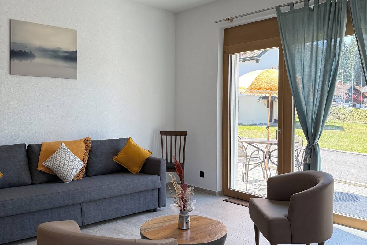 A modern living room with a grey sofa, two armchairs, a coffee table, and a painting on the wall.