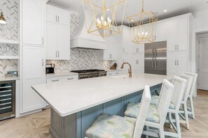 A modern kitchen with white cabinetry, a large island, and a stainless steel refrigerator.