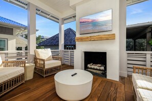 A spacious outdoor area with a fireplace, wicker furniture, and a large TV screen.
