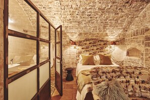 Une chambre rustique aux murs de pierre, avec un lit, une fenêtre à cadre en bois et une cheminée en pierre.