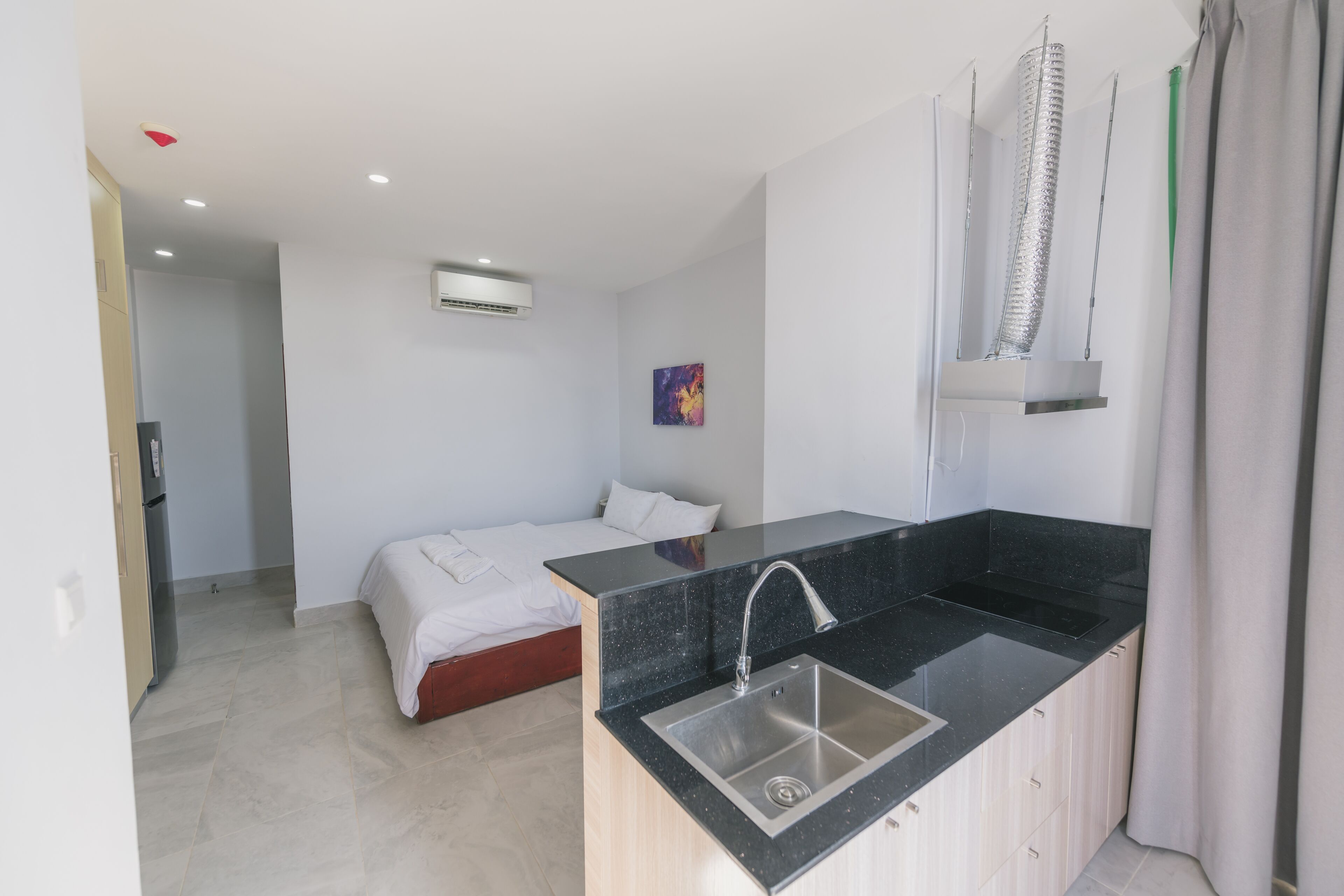 Habitación de hotel compacta con kitchenette, una cama, un baño pequeño y un cuadro en la pared.