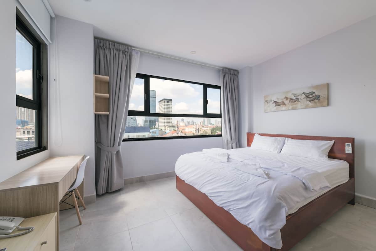 A modern hotel room with a large bed, a desk, and a window with a city view.